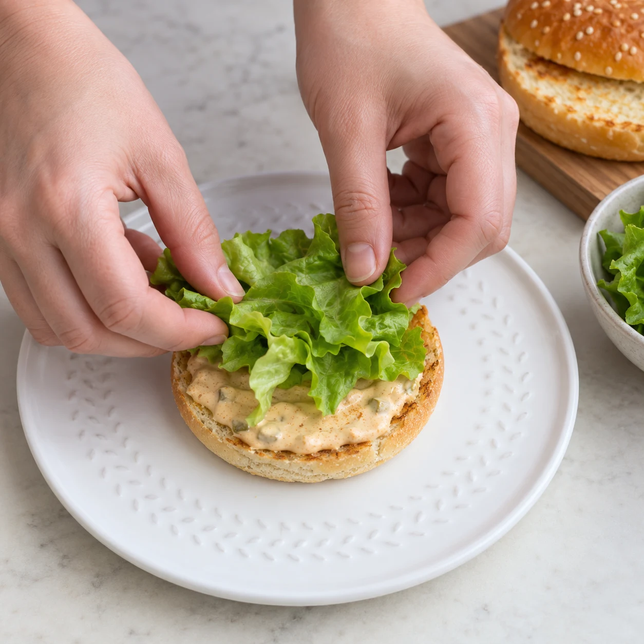 Une image carrée de l’action « Poser les feuilles de salade », avec seulement les ingrédients autorisés à cette étape, dans leur état réel. La salade est répartie sur les bases saucées. Mains anonymes si le geste le nécessite, aucun visage ni texte.