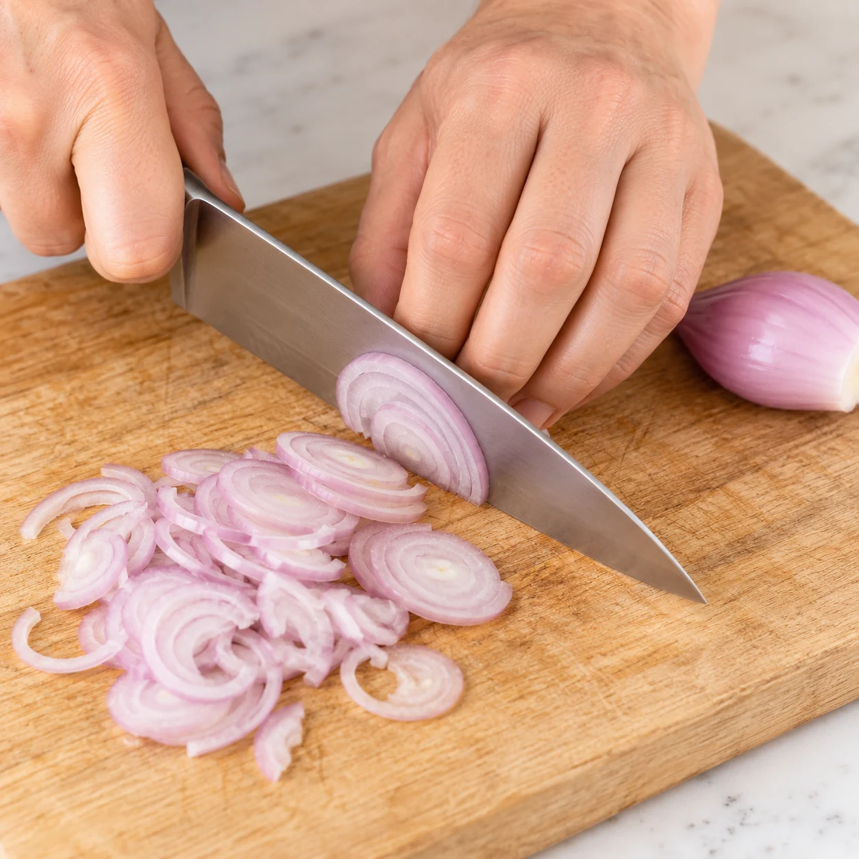 Une échalote seule émincée en rondelles fines, geste sûr sur planche stable. Les pâtes éventuelles de cette adaptation sont des coquillettes courtes jaunes courbées et creuses, pas des radiateurs.