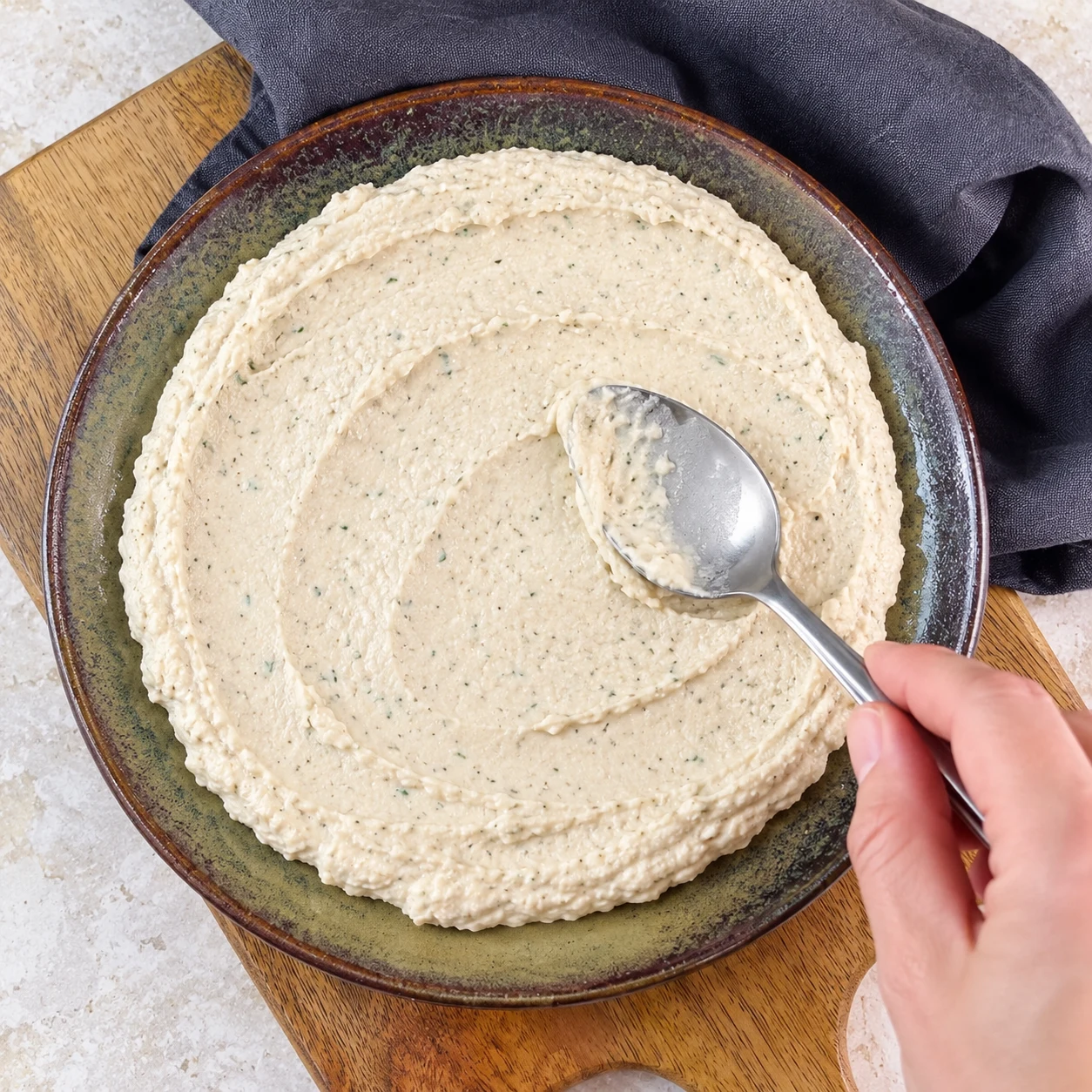 Cuillère étalant une crème pâle en couche épaisse sur assiette neutre ; pas encore de frites.