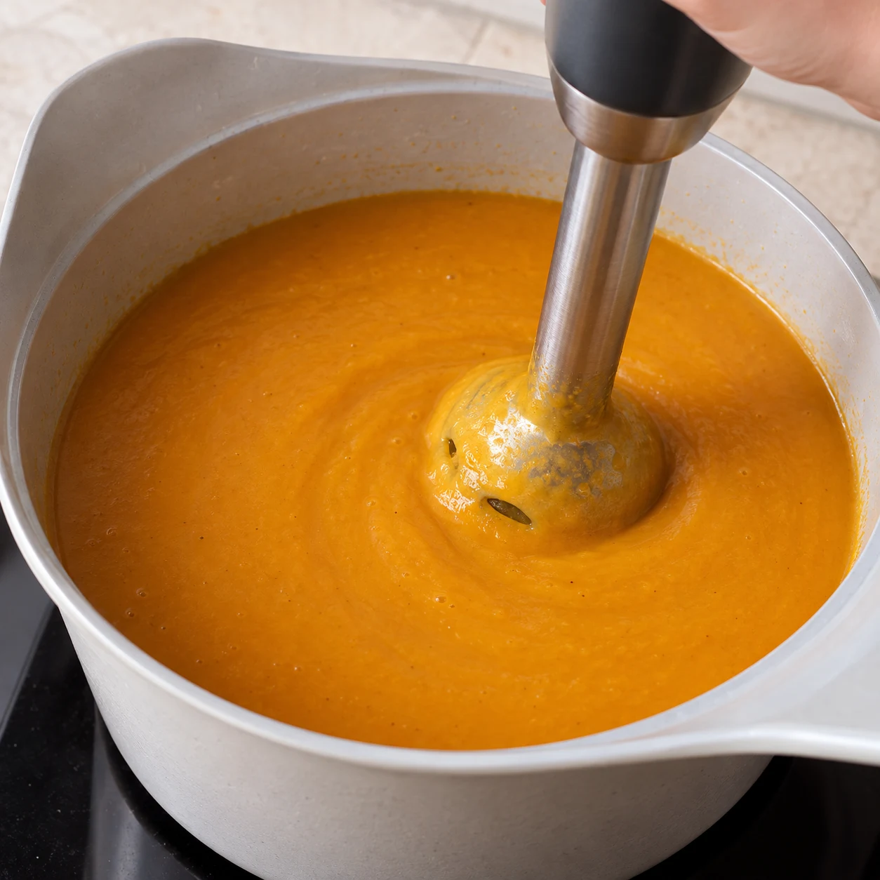 Mixeur plongeant immergé dans une soupe orange lisse.
