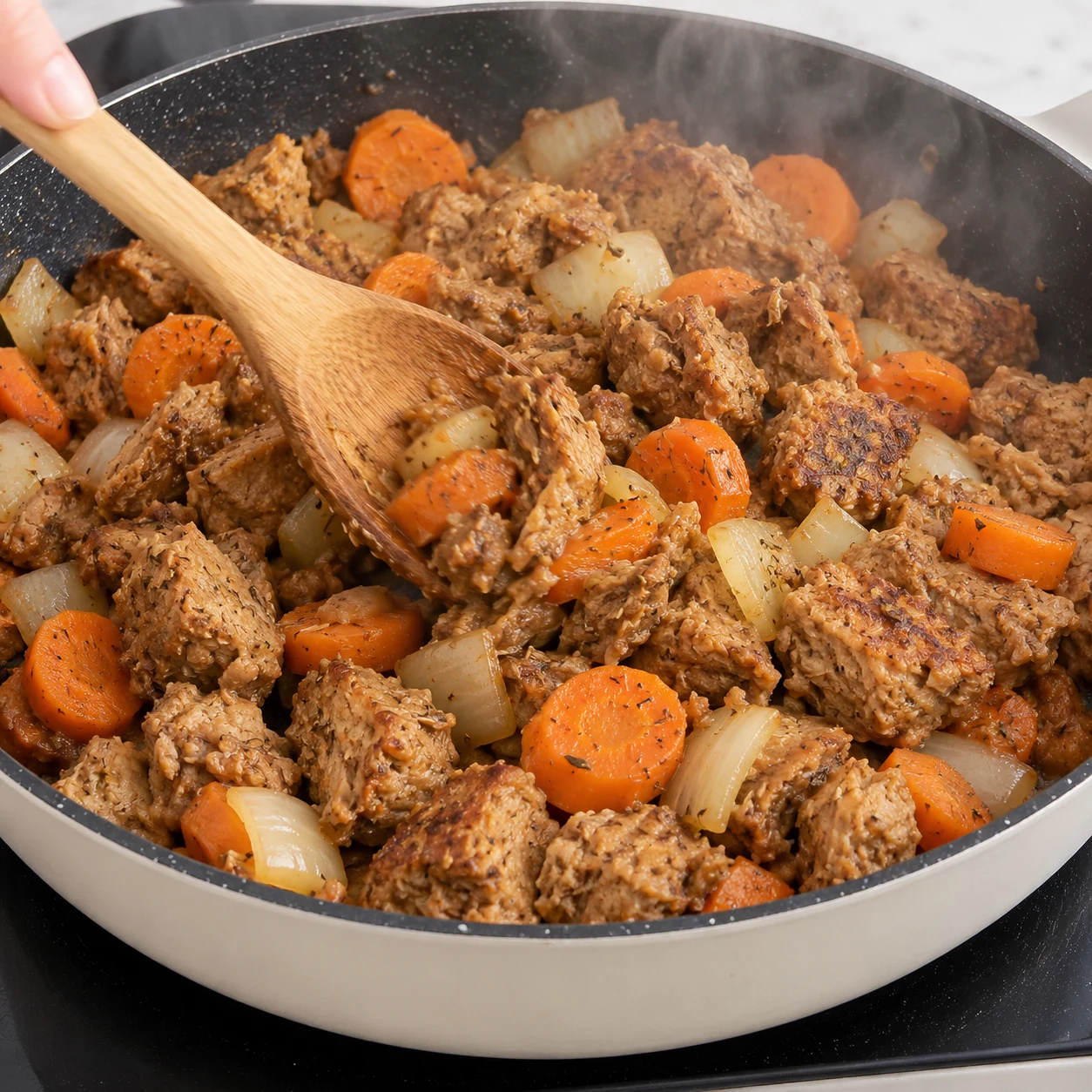 Morceaux de steak végétal dorés et légumes remués à la cuillère en bois dans la sauteuse fumante, farine absorbée.