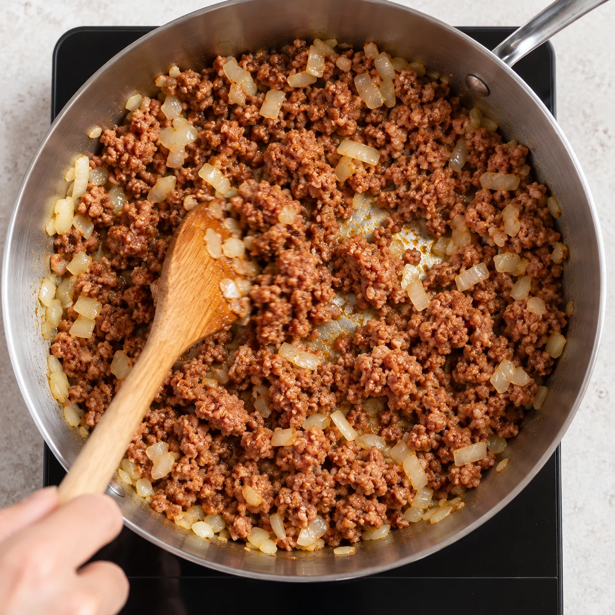 Haché végétal de soja brun légèrement tomaté mélangé avec l’oignon dans une poêle inox sur plaque; aucun bœuf cru.