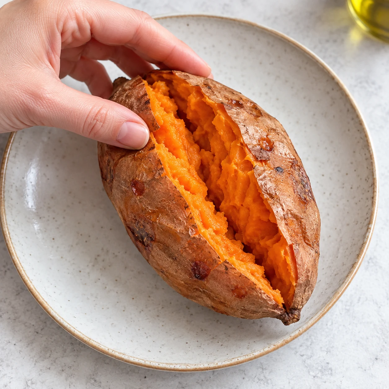 Ouvrir les patates douces : La patate douce est ouverte et sa chair orange est visible. Une seule scène correspondant à cette action, lumière naturelle claire sur pierre pâle, aucun texte ni personne identifiable.