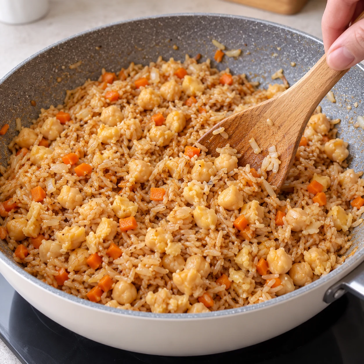 Mélangez tout le contenu de la sauteuse pour répartir le pois chiches dans le riz. État attendu : Les morceaux de pois chiches sont répartis dans le riz. Une seule scène de cuisine, sans personne identifiable.