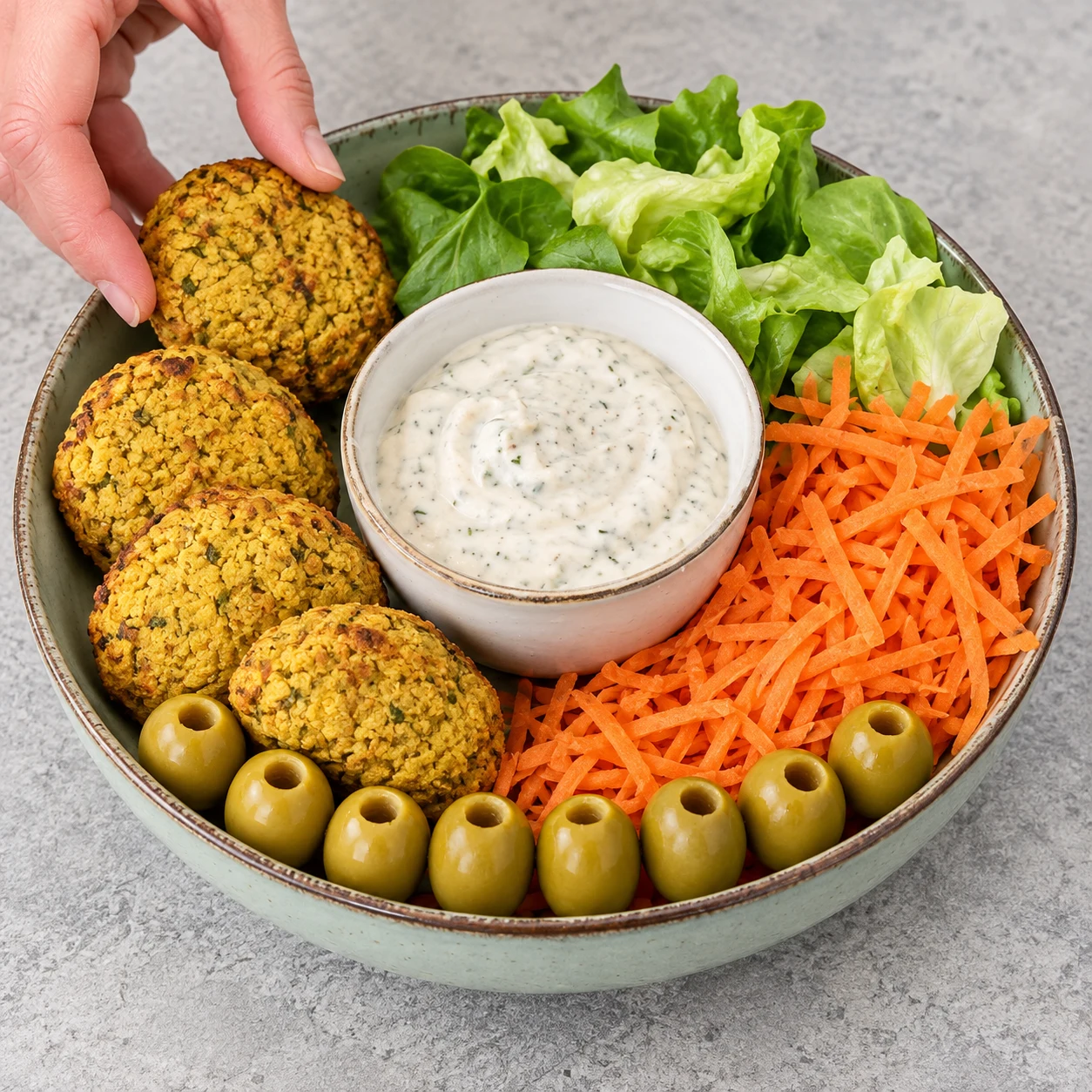 Assiette avec exactement quatre palets jaunes, un petit bol central de sauce au soja, huit olives vertes, salade verte et carotte râpée, sans fromage à cette étape.