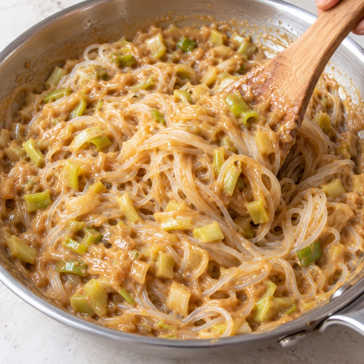 Vermicelles de riz blancs mélangés à la spatule en bois avec la sauce cacahuète et le poireau dans la poêle.