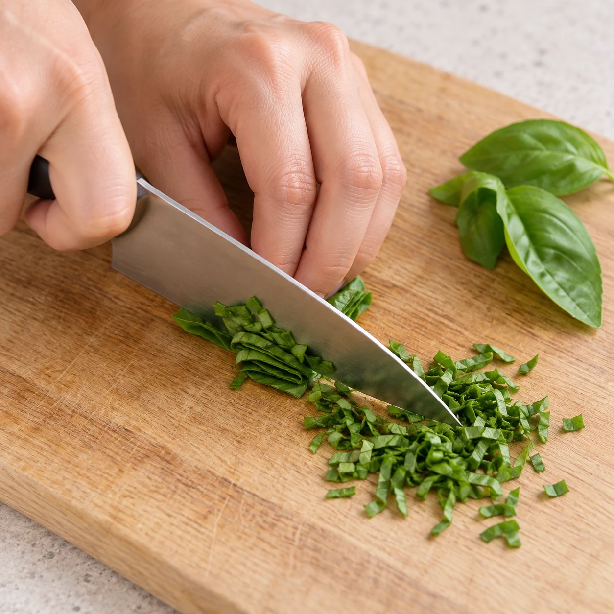 Ciselez les feuilles de basilic pour obtenir la pincée prévue. Montrer cette seule action et le résultat décrit, sans texte.