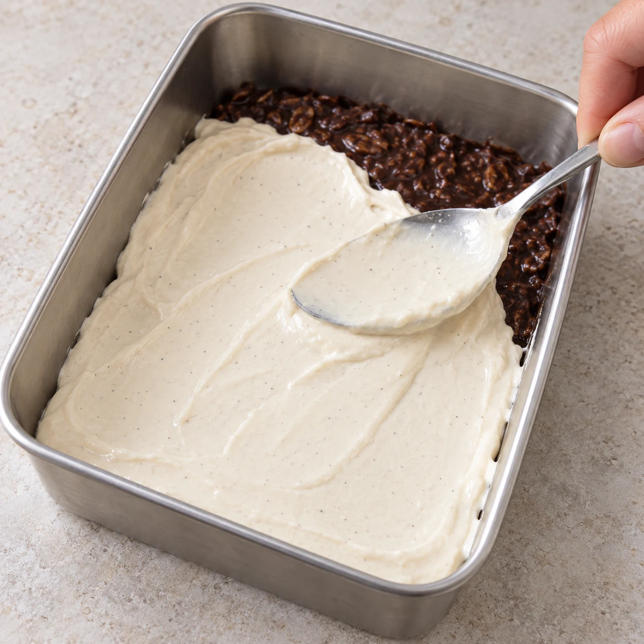 Moule en inox dont la surface est couverte d'une couche lisse de crème beige clair étalée au dos d'une cuillère.