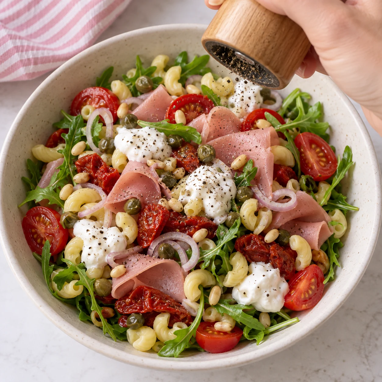 Main anonyme saupoudrant légèrement le poivre noir sur salade montée avec jambon végétal et yaourt soja. Les pâtes éventuelles de cette adaptation sont des coquillettes courtes jaunes courbées et creuses, pas des radiateurs.