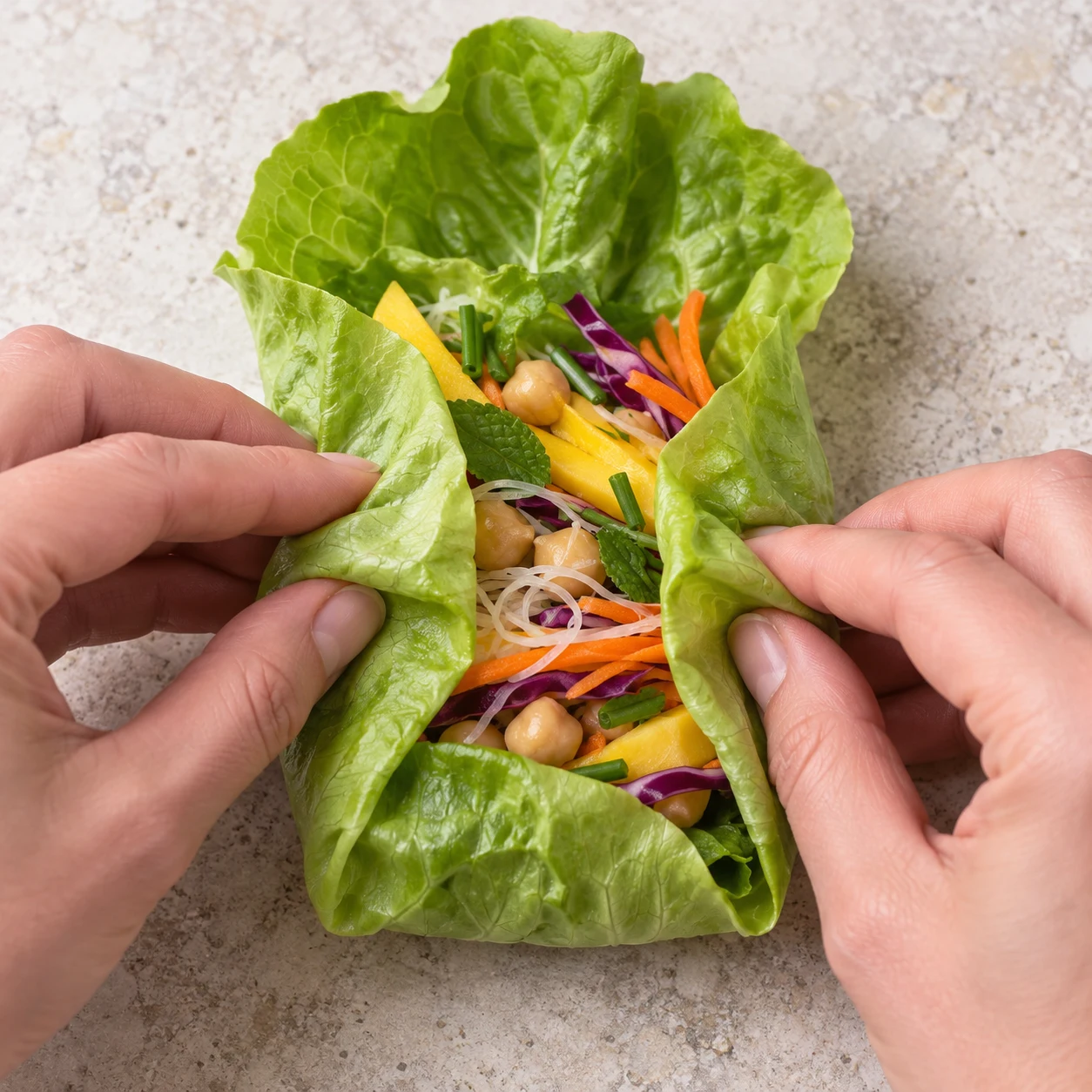 Une seule action : Rabattre les côtés. Les deux extrémités sont retenues par les côtés repliés. Seulement Laitue blonde fraîche en grandes feuilles, Menthe fraîche, Salade verte, Carotte, Chou rouge, Mangue bien mûre, Ciboulette fraîche, Vermicelles de riz secs, Pois chiches cuits égouttés. Toute enveloppe est de la laitue verte opaque. Supprimer toute feuille de riz et toute crevette de la capture de référence. Le geste vient de l’adaptation explicitement documentée, pas du geste filmé.