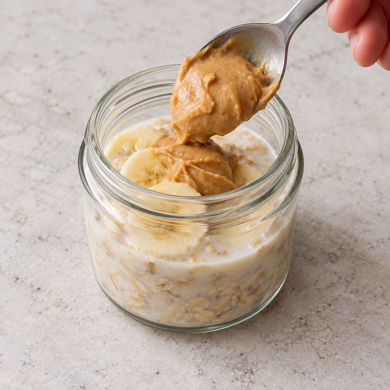 Une cuillère dépose une noisette généreuse de purée de cacahuète beige dans le bocal humide.