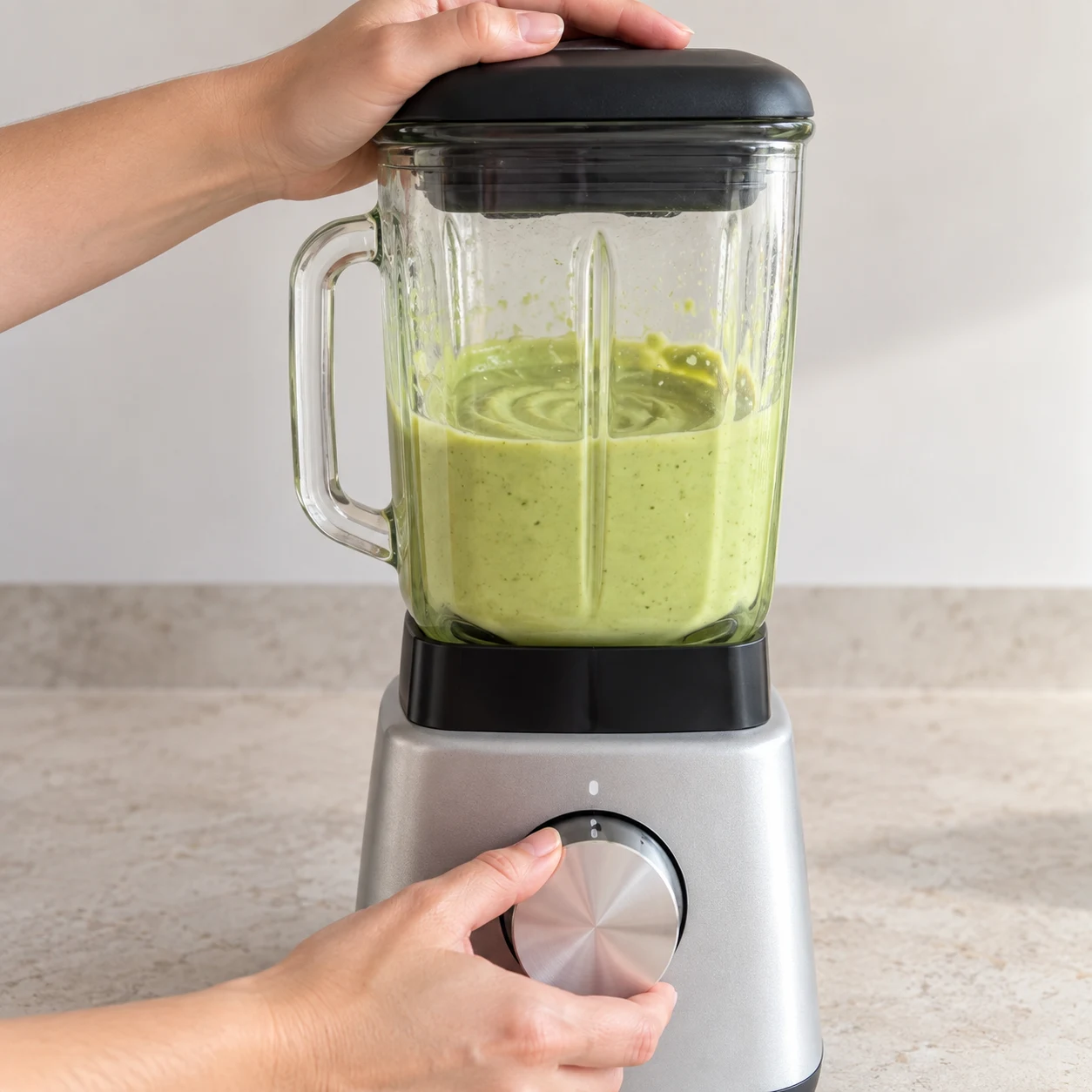 Mixeur fermé contenant une crème vert pâle lisse; mains anonymes actionnant le bouton.