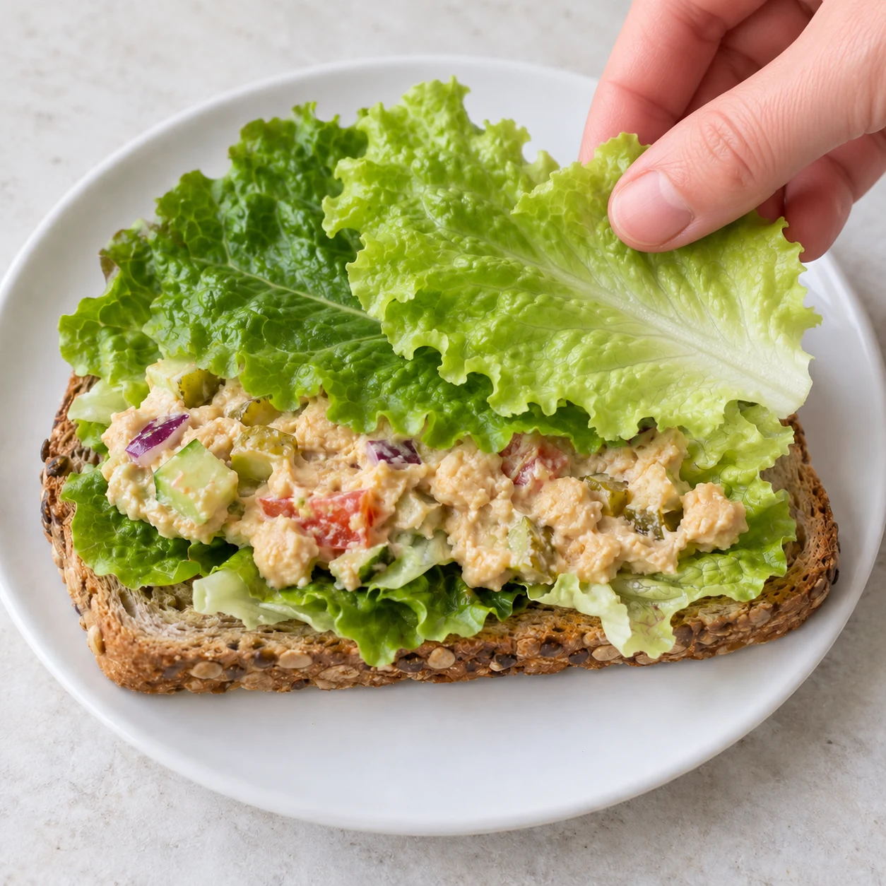 Posez les 2 feuilles de salade restantes sur la première couche de garniture. Montrer uniquement les ingrédients de cette phase sur pierre pâle, vaisselle blanche neutre.