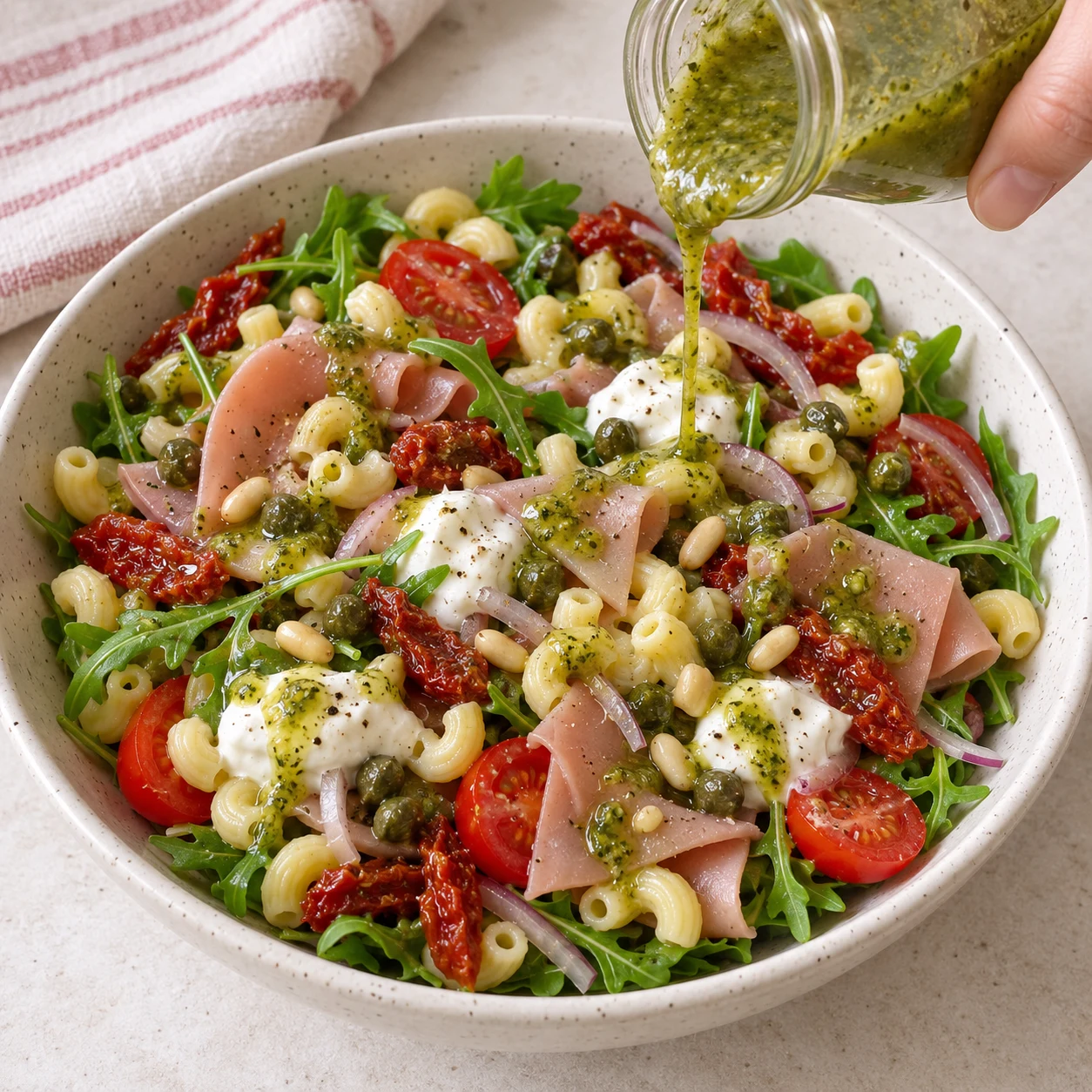 Bocal versant un mince filet de sauce verte sur salade finale entièrement végétale, pas de légumes supplémentaires. Les pâtes éventuelles de cette adaptation sont des coquillettes courtes jaunes courbées et creuses, pas des radiateurs.