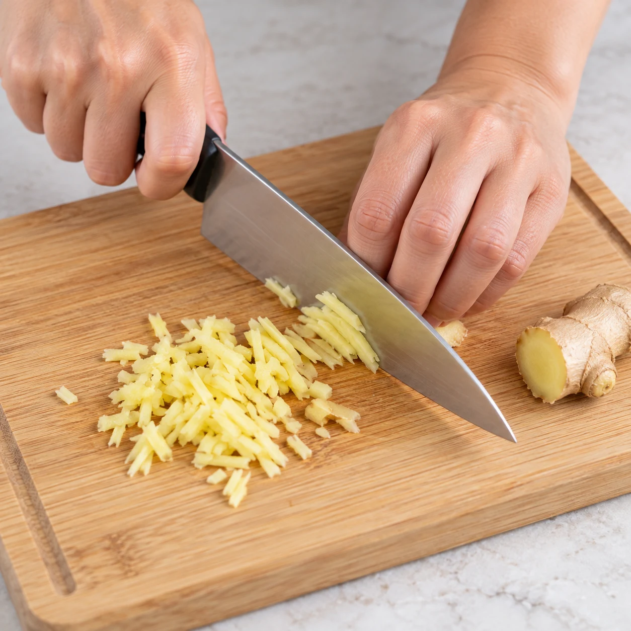 Découpe sûre de gingembre frais beige en petits morceaux sur une planche stable.