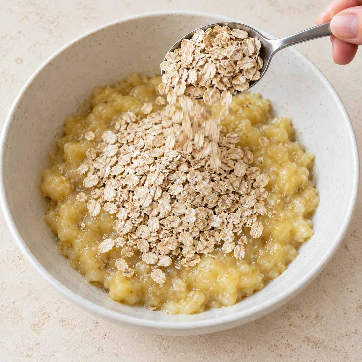 Ajoute les 8 cuillères à soupe de flocons d’avoine sur la purée de banane. État attendu : Les 8 cuillères de flocons sont déposées sur la purée.