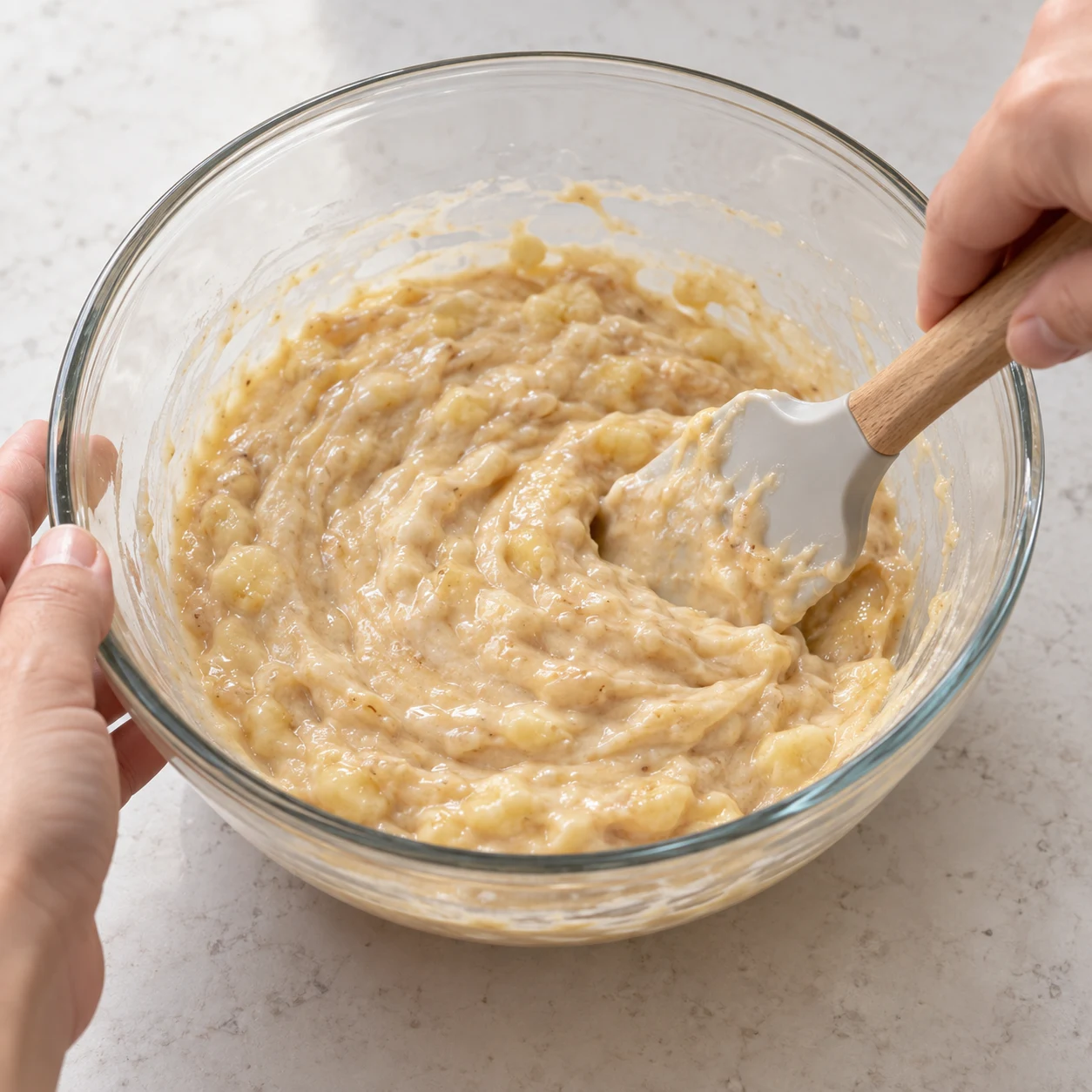 Une spatule mélange la purée de banane, le yaourt soja blanc et la purée de cacahuète beige.