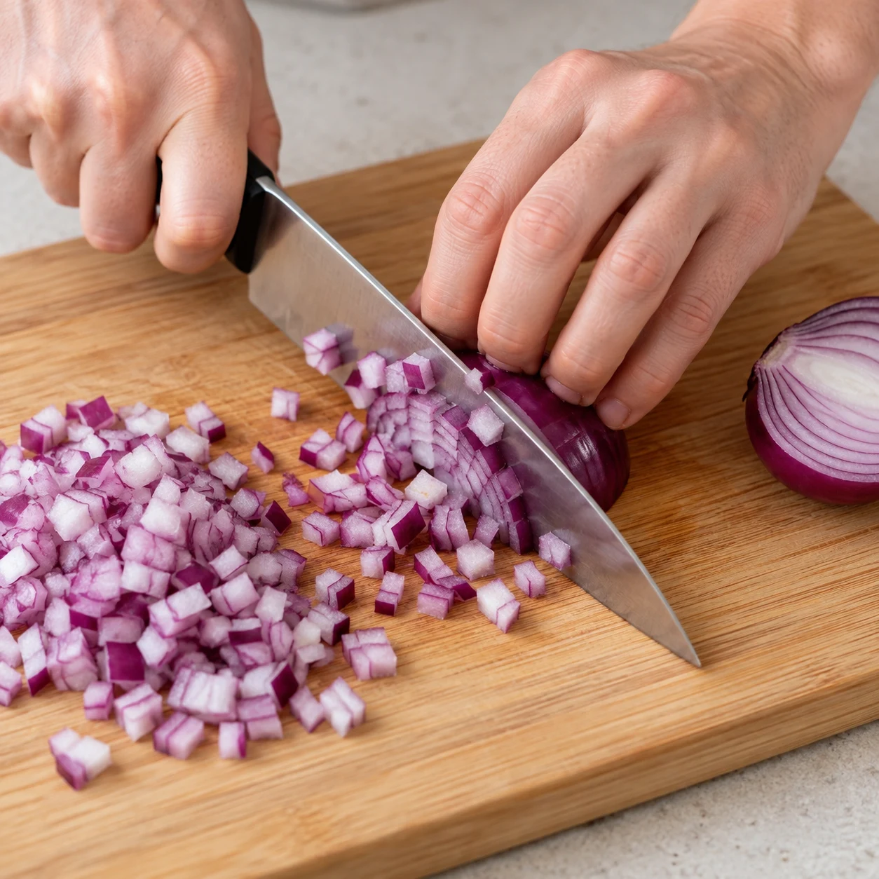 Découpe active d’un oignon rouge en petits dés, main en griffe, sans autres légumes.