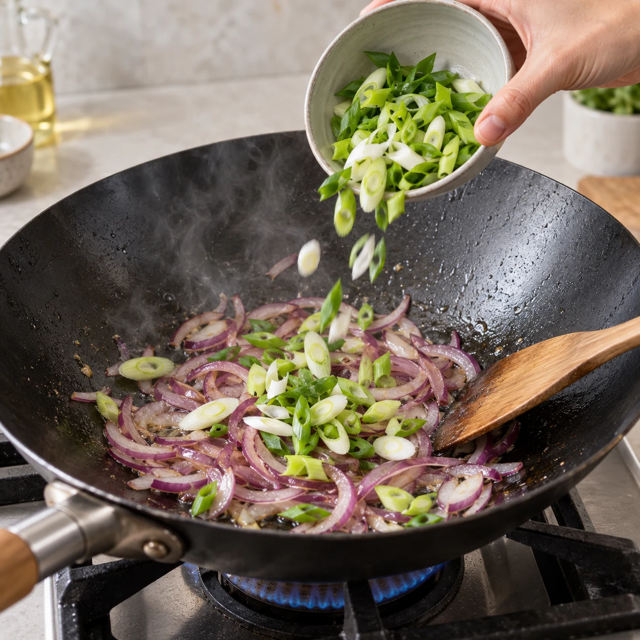 Ajouter la cébette — La cébette est répartie avec l’oignon dans le wok.