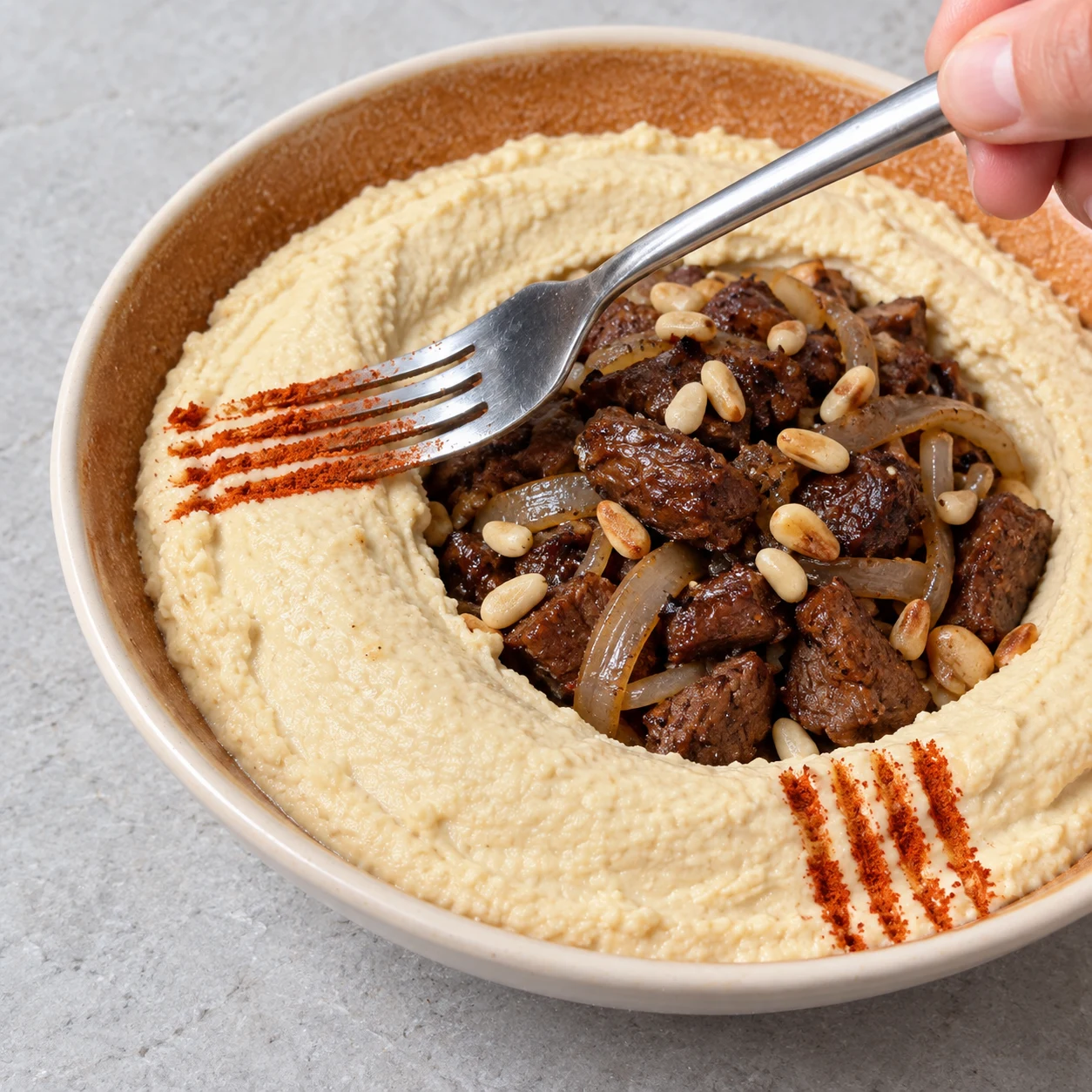 Déposer une pointe de paprika sur le houmous avec les dents d’une fourchette. Montrer seulement les ingrédients de cette phase, dans une mise en scène claire et anonyme.
