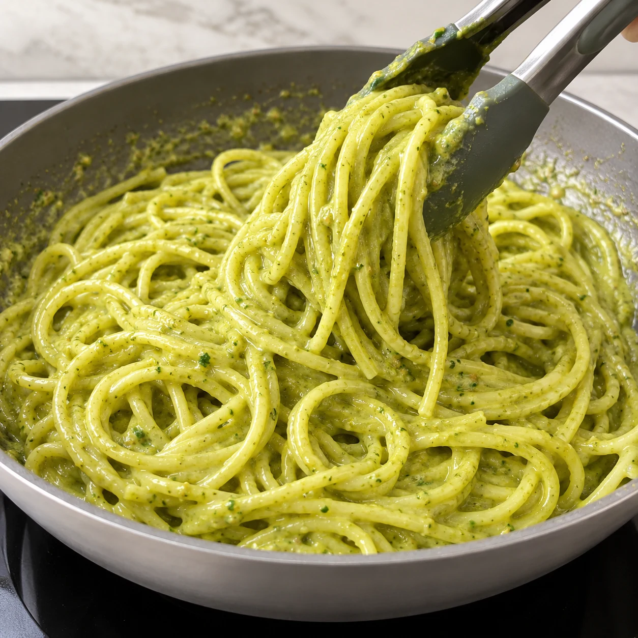 Spaghetti verts brillants remués avec une pince dans la poêle, sauce crémeuse sans garniture finale.