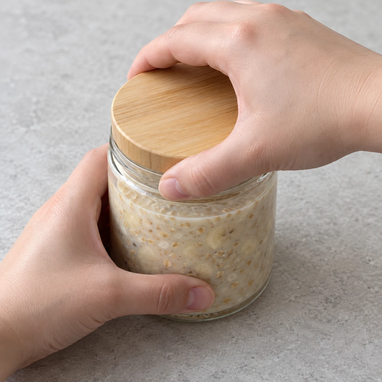 Une main ferme un bocal en verre avec un couvercle sobre, mélange encore assez liquide.