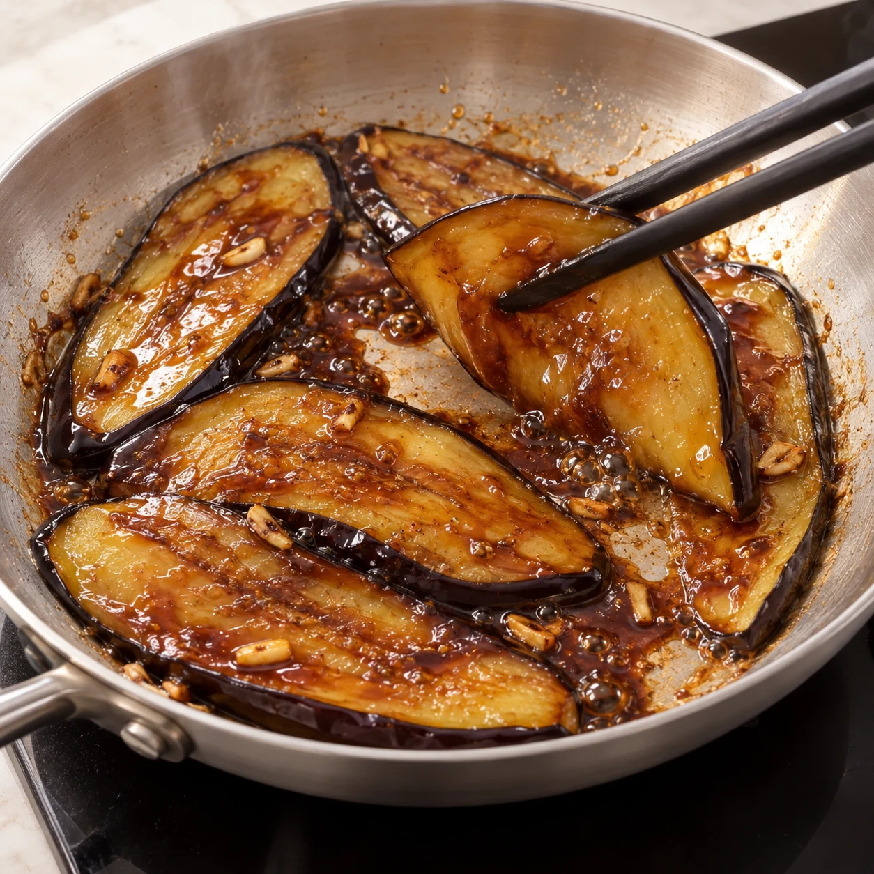 Ajoute la sauce soja sucrée aux aubergines. Retourne les lamelles dans la sauce et laisse caraméliser quelques minutes, sans laisser noircir le fond. Résultat visible : La sauce nappe les lamelles et devient brillante, sans odeur de brûlé.
