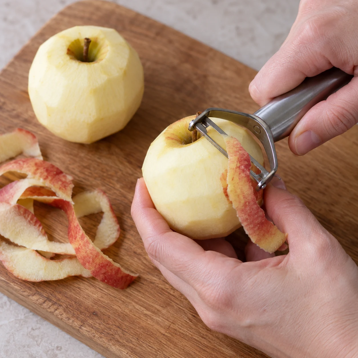 Main anonyme épluchant une petite pomme sur une planche stable.