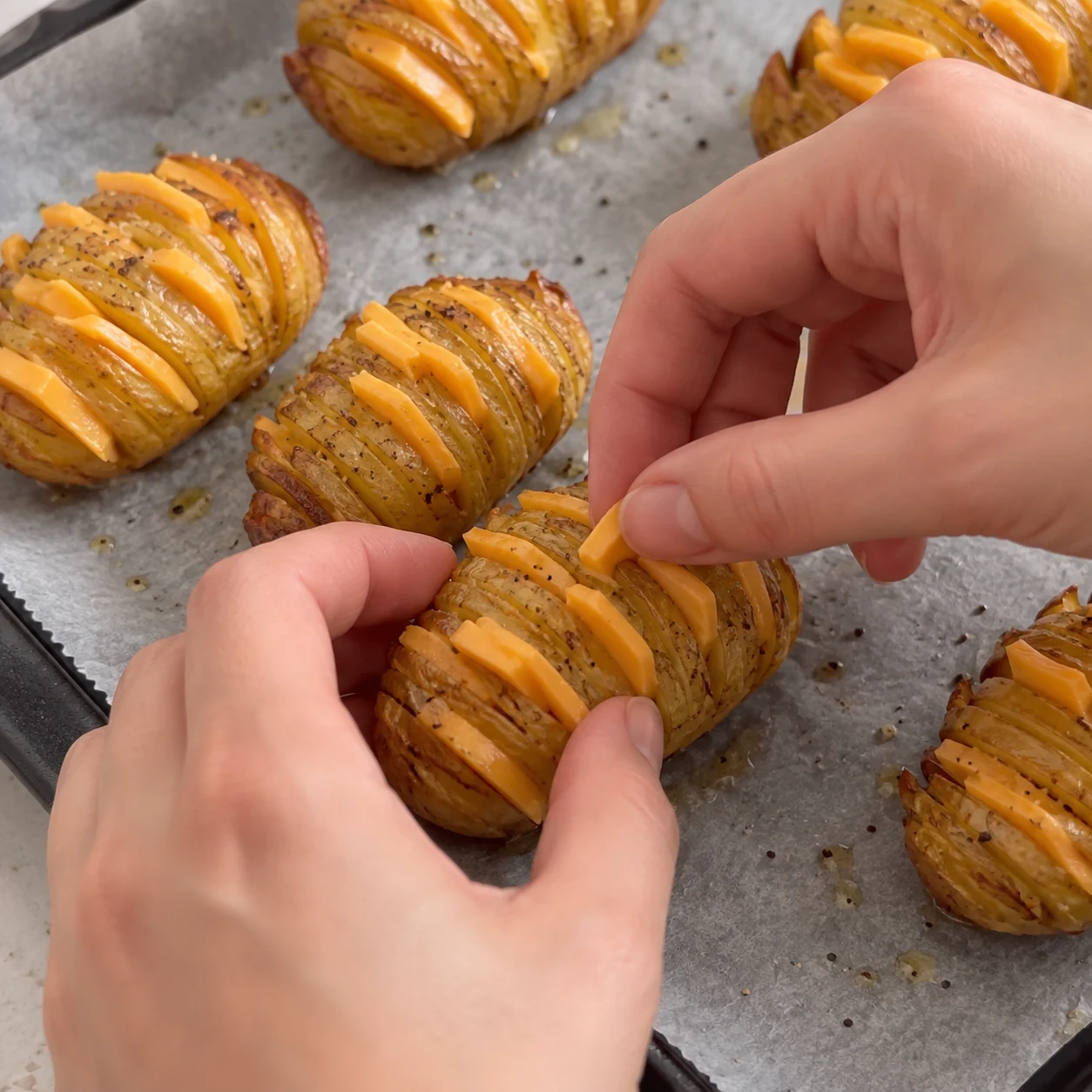 Mains anonymes insérant de fines bandes orangées de fromage végétal dans les pommes de terre cuites ; aucun lardon encore.