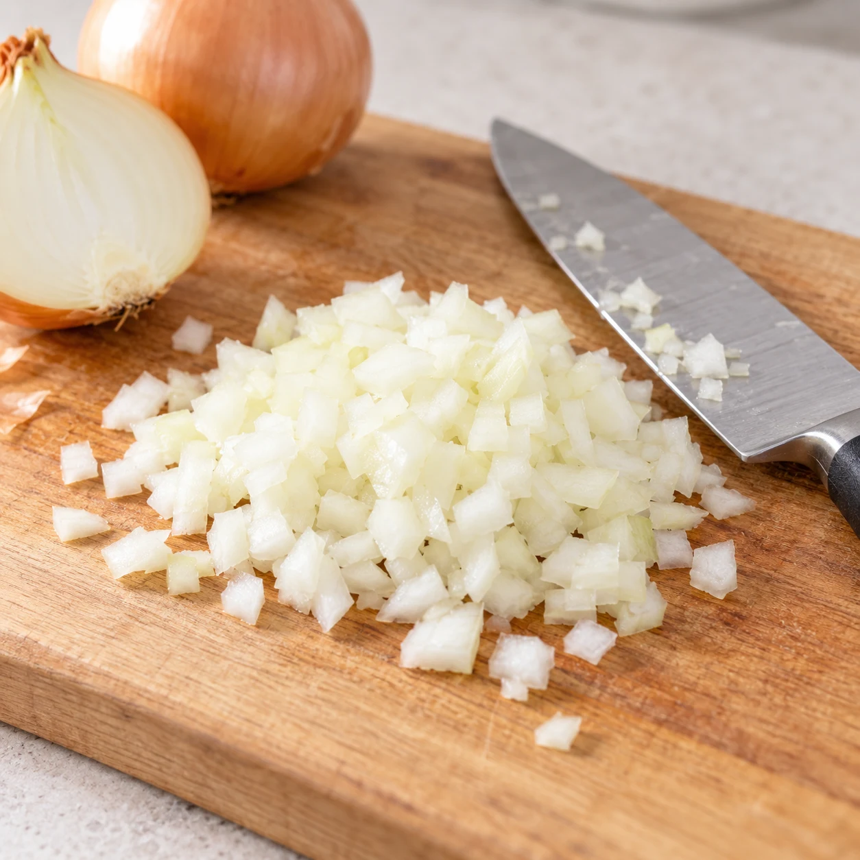 Oignon jaune haché en petits dés sur une planche, couteau de cuisine à côté.