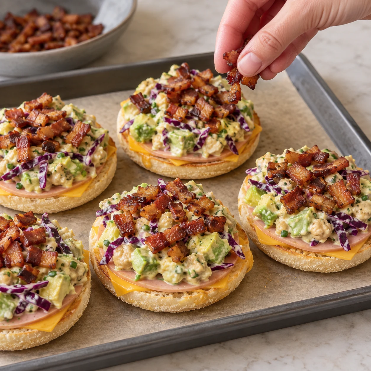 Petits lardons végétaux fumés dorés déposés sur la farce colorée d’un muffin anglais ouvert ; forme en lardons, jamais deux bandes entières.