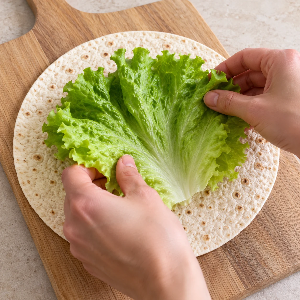 Mains anonymes déposant une feuille de laitue sur une tortilla plate.