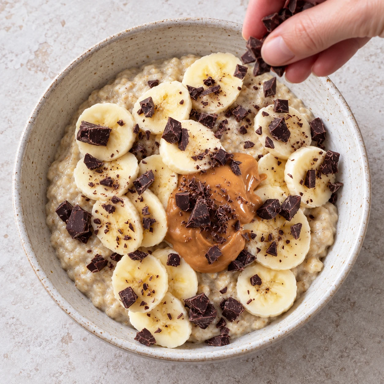 Petits éclats de chocolat noir répartis sur le porridge, la banane et la cuillerée de beurre de cacahuète.