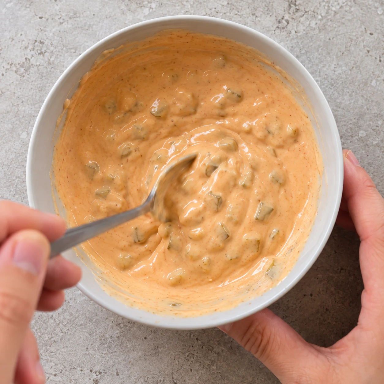 Cuillère mélangeant une sauce orangée crémeuse dans un bol.