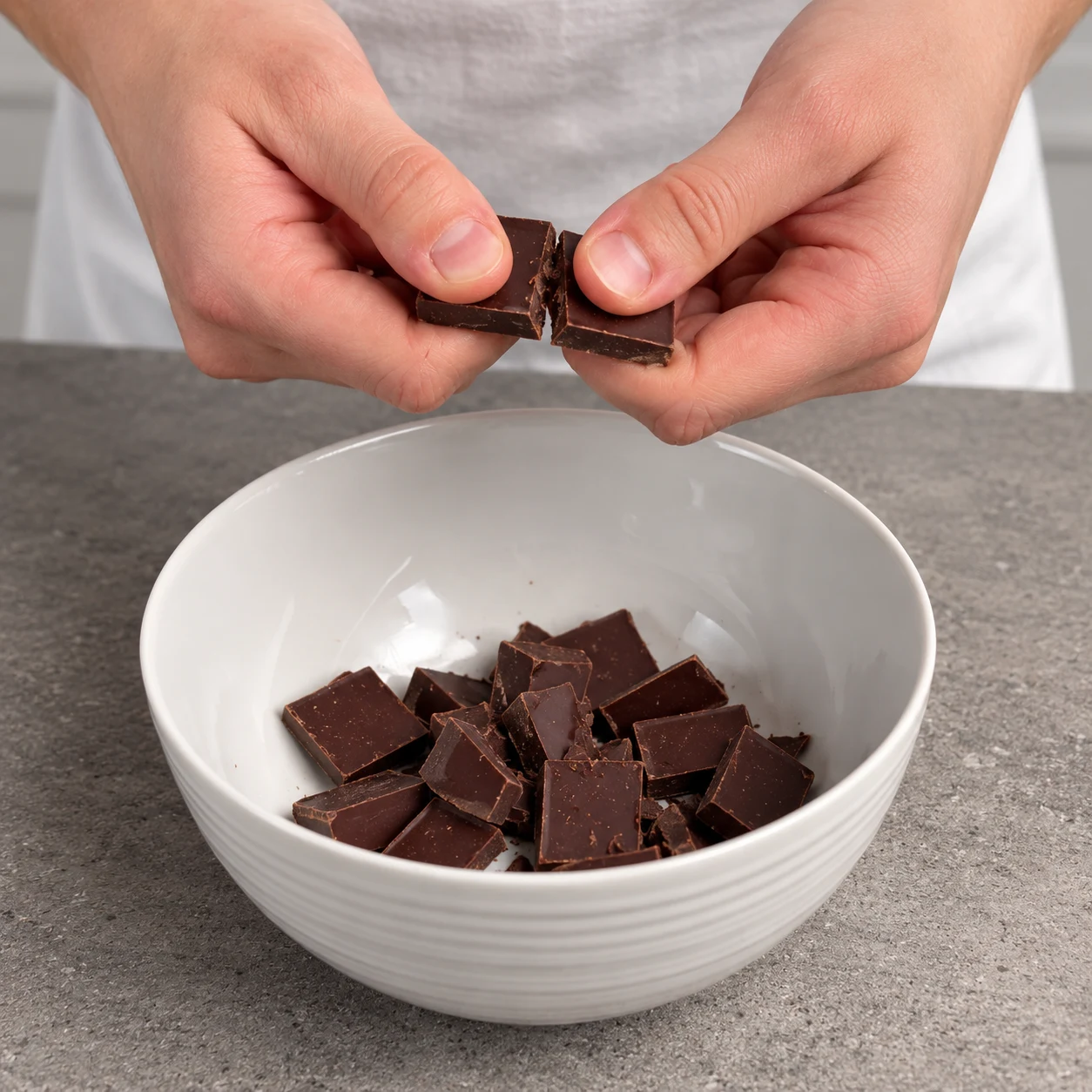 Casse les 100 g de chocolat noir en morceaux dans un bol. État à montrer : Le chocolat est en morceaux dans le bol.