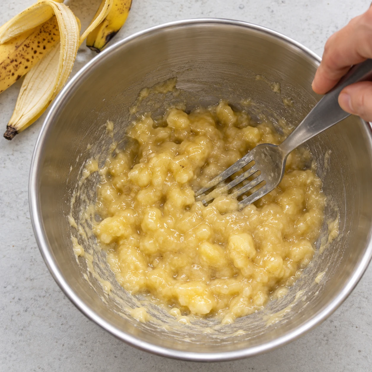 Une fourchette écrase les bananes dans un saladier inox.