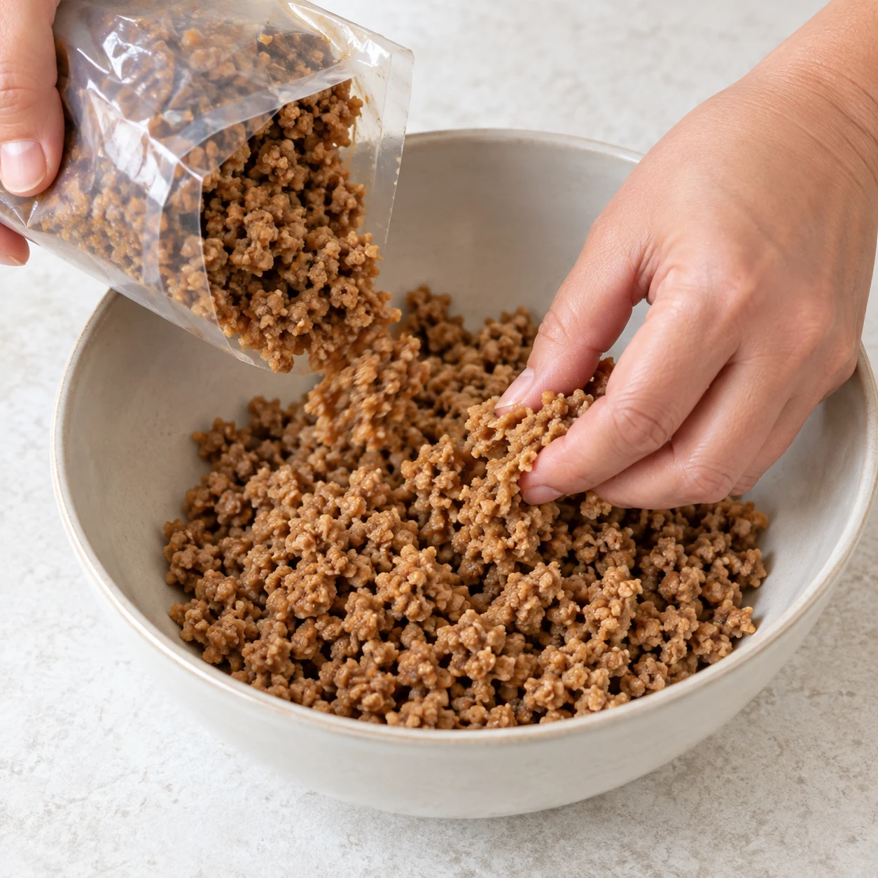 Ouvre le sachet de haché de soja cuisiné et sépare délicatement les morceaux dans le saladier. Résultat : Les morceaux de haché de soja sont séparés dans le saladier.