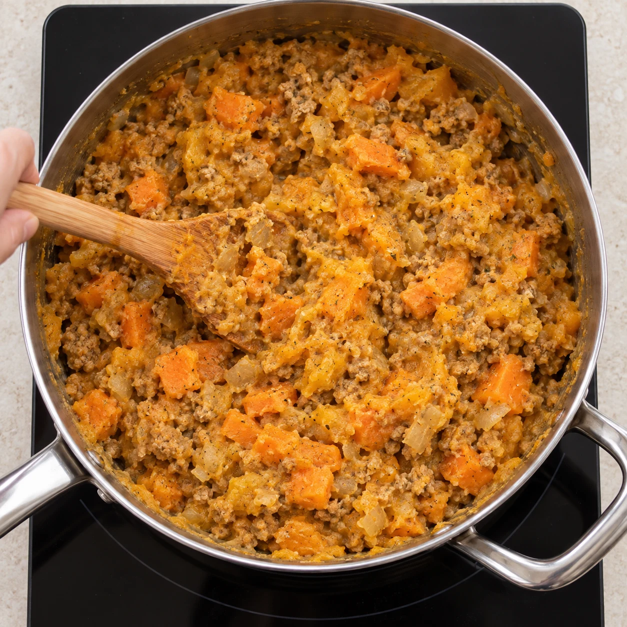 Farce orange de courge et patate douce mêlée de haché végétal brun et d’oignon, remuée à la spatule dans une poêle inox; pas encore de fromage.