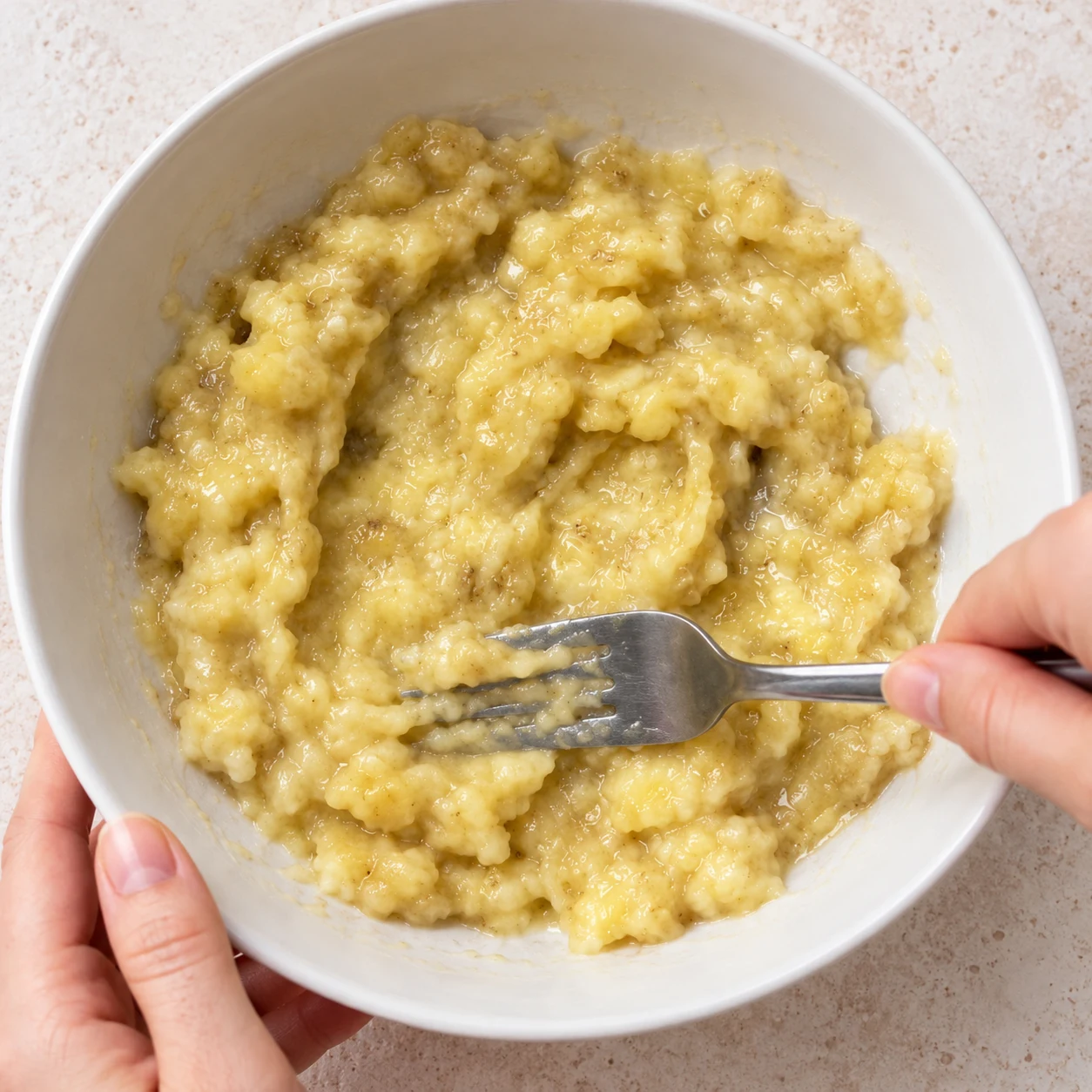 Écrase les 2 bananes bien mûres et épluchées dans un saladier avec une fourchette. État attendu : La chair est écrasée en une purée humide, sans gros tronçons.