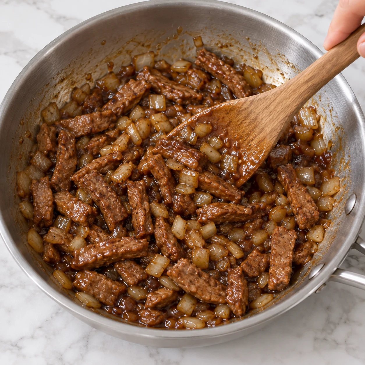 Main anonyme mélangeant une sauce soja-érable brillante aux lamelles végétales et à l’oignon, sans nouilles ni carottes.