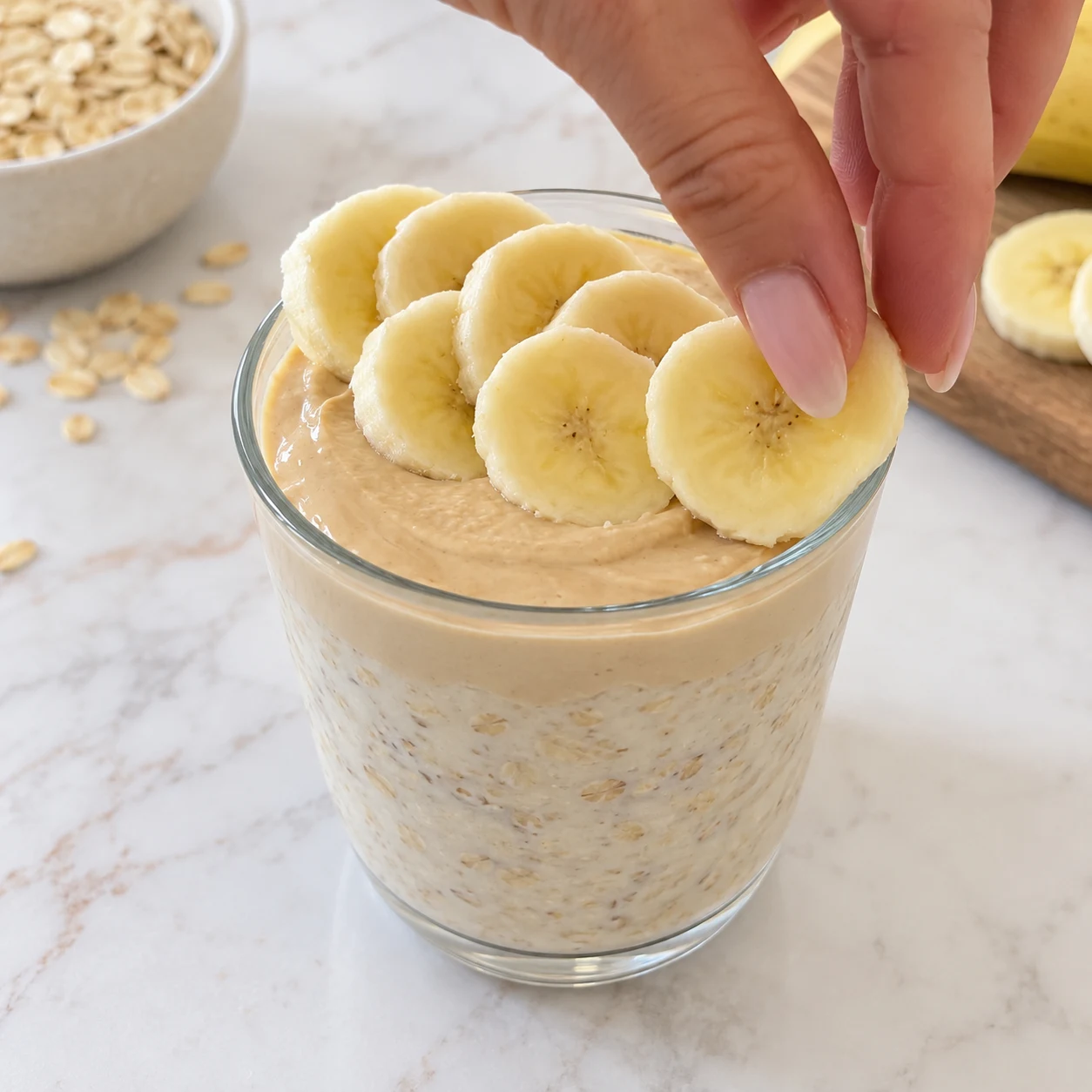 Main anonyme posant une rondelle de banane au-dessus de la crème, sans cacahuètes.