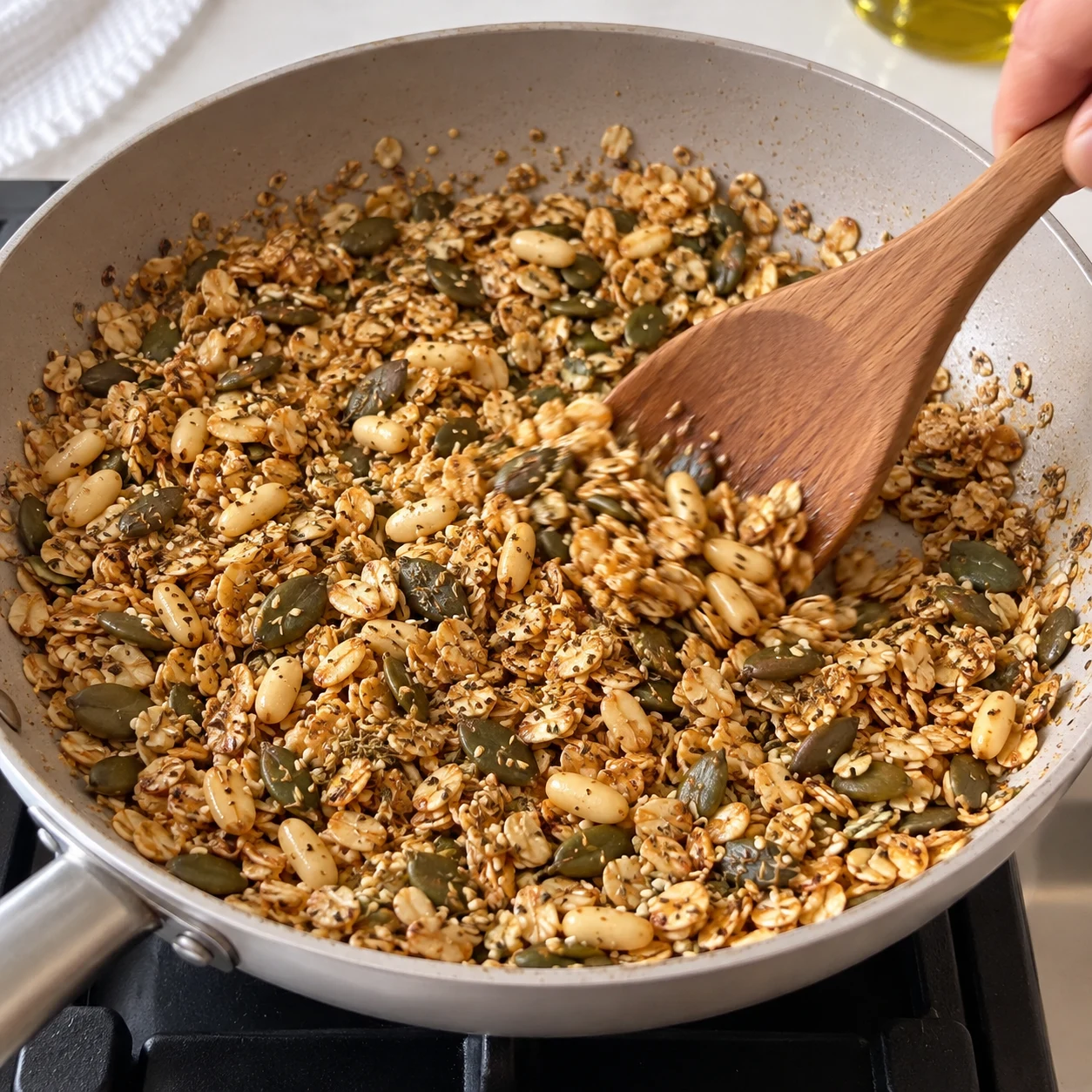 Fais cuire 5 min en mélangeant constamment le granola dans la poêle. Ne montrer que le granola, aucune tomate ni base blanche. Geste décrit par la recette d’origine, non filmé.