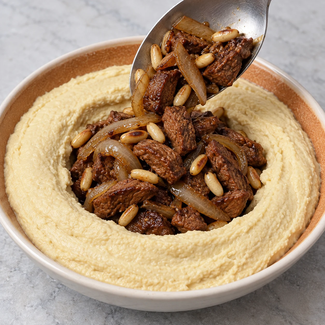 Déposer la garniture végétale chaude et les pignons au centre du houmous. Montrer seulement les ingrédients de cette phase, dans une mise en scène claire et anonyme.