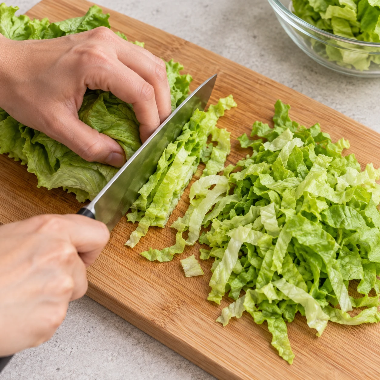 Une seule photographie carrée du geste « Couper la salade »: Émince les 130 g de salade propre et bien égouttée sur une planche stable. État obtenu: La salade est découpée en petites lanières et ne porte plus d’eau visible.. Uniquement les ingrédients autorisés à cette étape; pas de visage, de texte ou d’ingrédient animal.