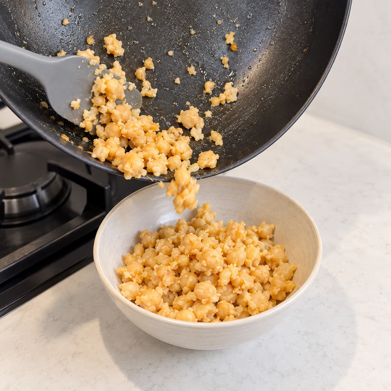 Une seule photo carrée montrant réserver les pois chiches. Les pois chiches sont dans un bol hors du wok. Seulement les ingrédients déjà présents : Pois chiches cuits égouttés, Huile de tournesol. Les éclats sont beige de pois chiches, sans œuf, sans tofu et sans purée lisse.