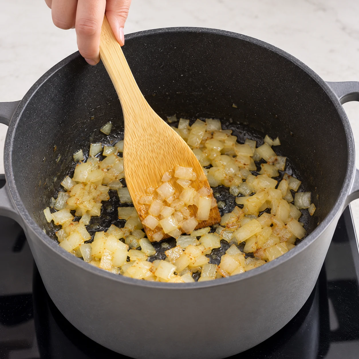 Spatule remuant des morceaux d’oignon blondis au fond de la cocotte.
