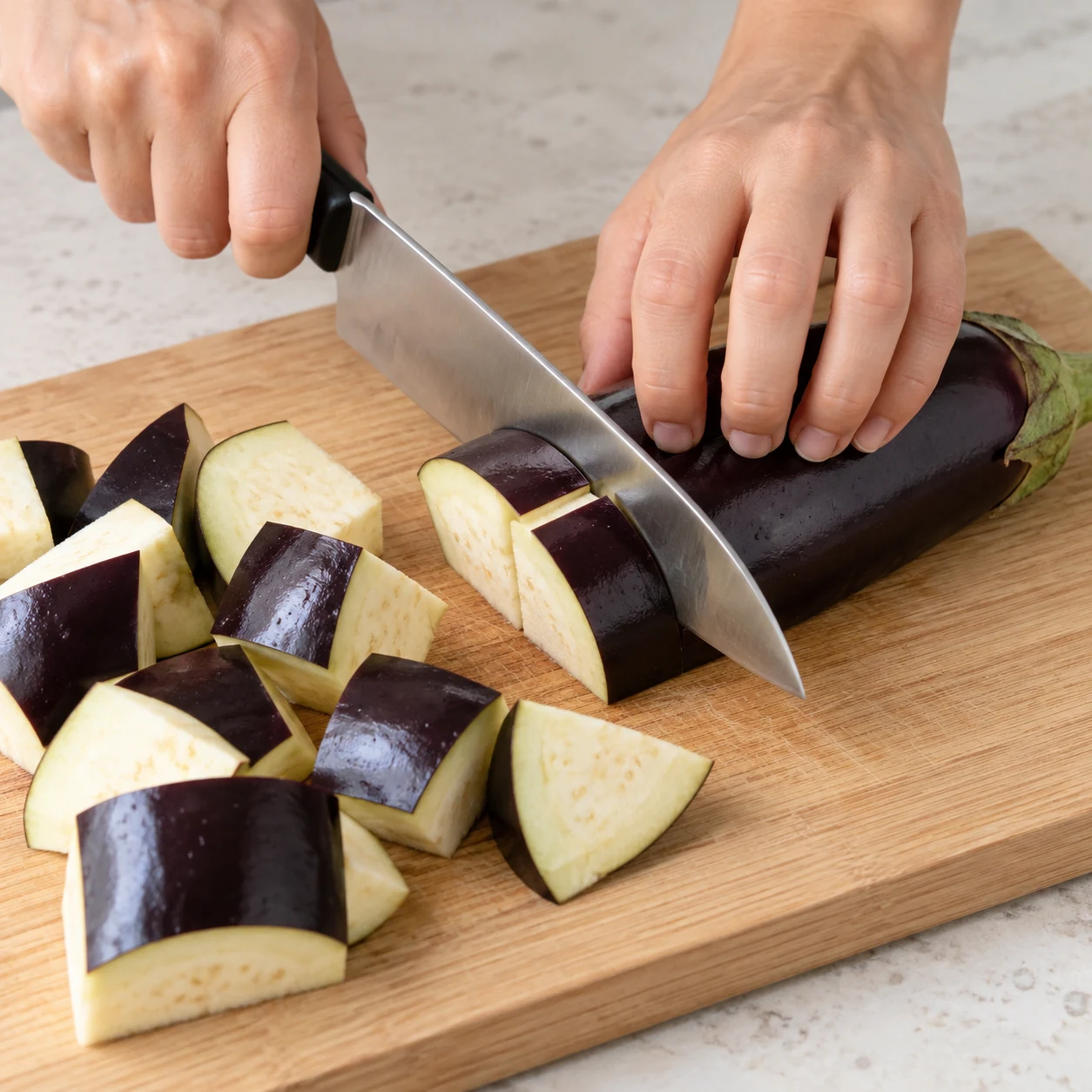Mains anonymes coupant une aubergine en gros morceaux, lame sûre et prise en griffe.