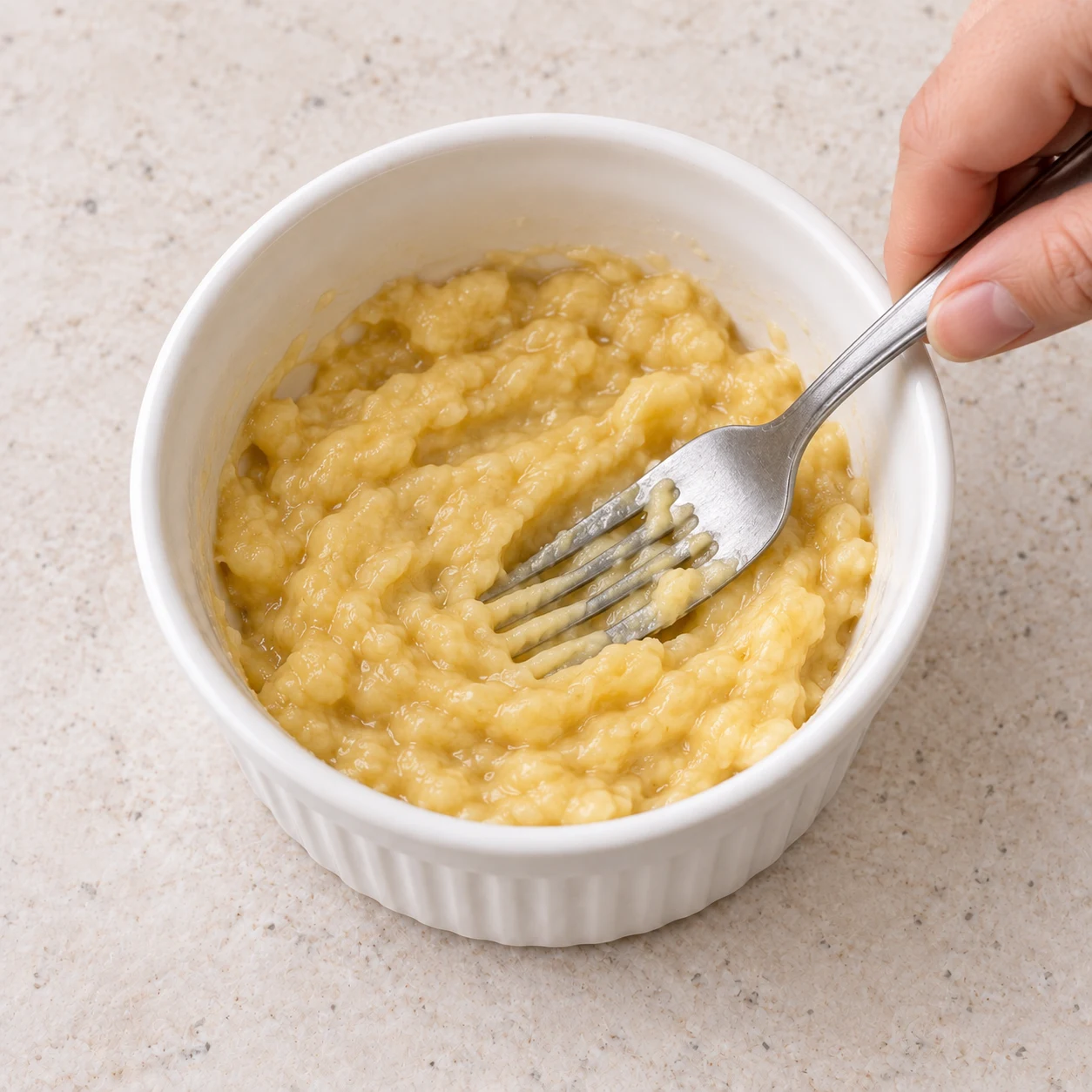 Une fourchette écrase une purée jaune de banane dans un petit bol blanc, sans aucun œuf.