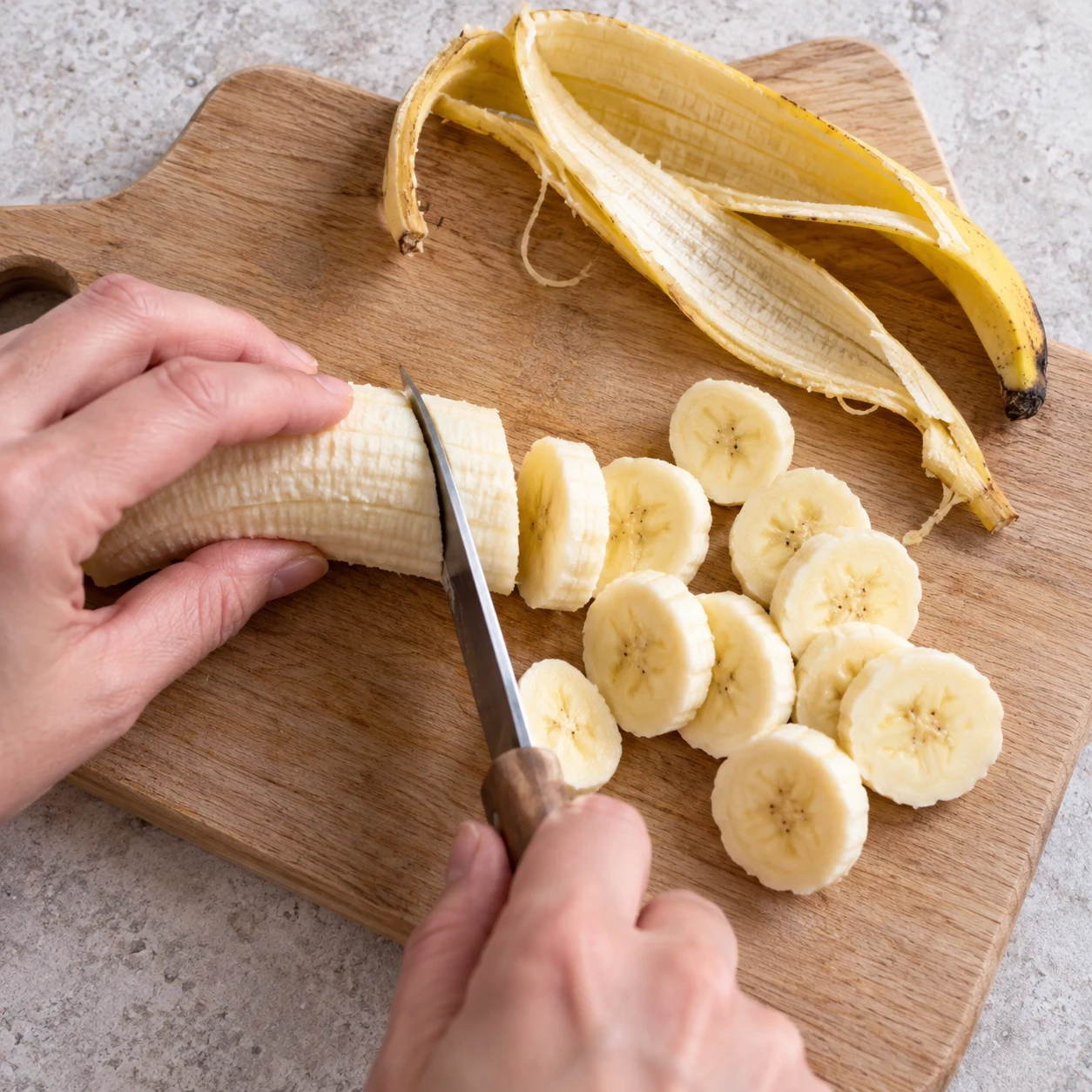 Mains anonymes, prise sûre, rondelles de banane sur planche stable.