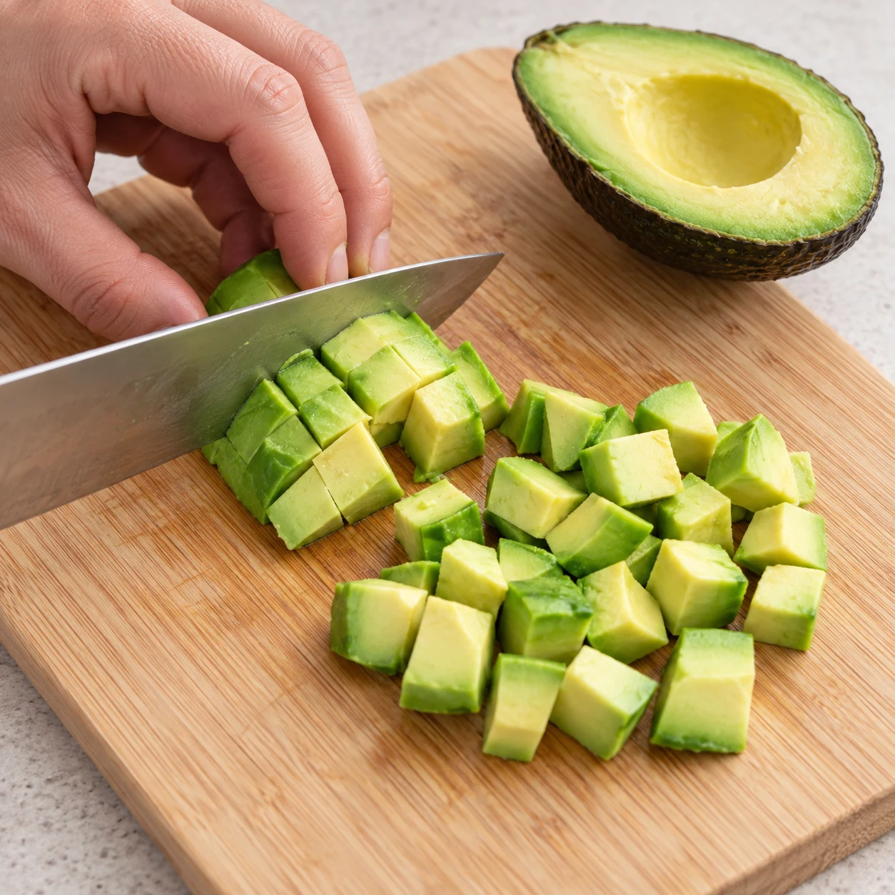 Retirez la peau et le noyau de l’avocat, puis coupez sa chair en dés, comme ceux ajoutés dans le saladier.